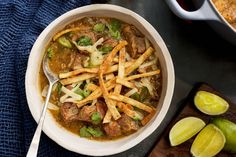 a bowl filled with meat and french fries next to some sliced limes on a cutting board