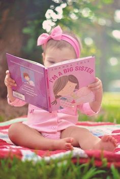 a baby girl reading a book on the ground with her pink outfit and headband