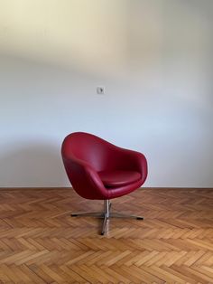 a red chair sitting on top of a hard wood floor next to a white wall