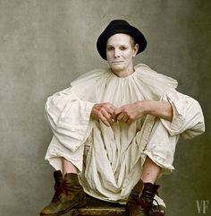 a man sitting on top of a suitcase wearing a white shirt and black hat with his legs crossed