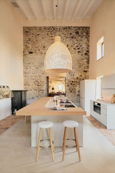 a large kitchen with two stools in front of the island and stone wall behind it