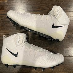 a pair of white nike cleats sitting on top of a wooden floor