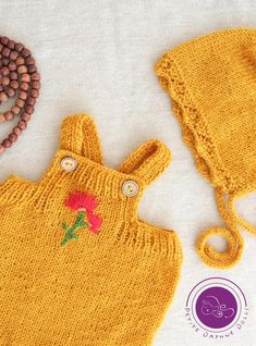 a yellow knitted outfit with flowers on the front, and a beaded necklace next to it