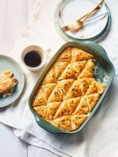 a casserole dish on a table next to two plates and a cup of coffee