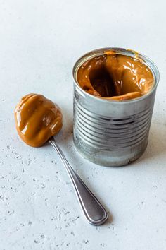 a can of peanut butter next to a spoon on a white counter top with some peanut butter in it