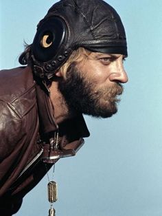 a man wearing a leather jacket and helmet with an eye patch on his forehead, looking to the side