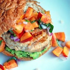 a chicken burger with lettuce, tomato and onions on a blue plate next to sliced peaches