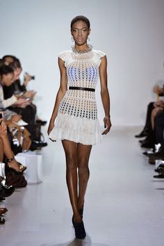 a model walks down the runway in a short white dress with crochet detailing