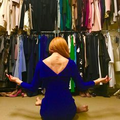 a woman sitting on the floor in front of a closet full of shirts and dresses