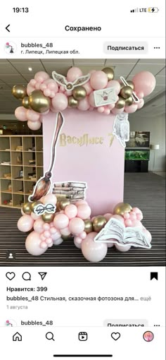 a pink and gold balloon arch with balloons on it in the middle of a room