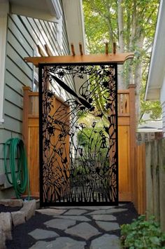 an open gate in front of a house with trees and bushes on the side walk