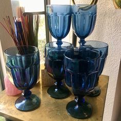 four blue glasses sitting on top of a table next to a vase with sticks in it