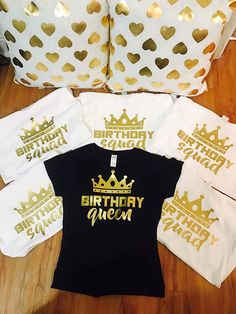 four birthday shirts with gold foil on them sitting on a wooden floor next to pillows