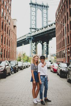 a man and woman are standing in the middle of an alleyway under a bridge