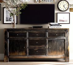 a tv is sitting on top of an old dresser in front of a wall with clocks