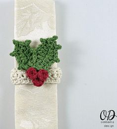 a crocheted christmas tie with holly and red berries on white fabric, hanging from a hook