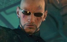 a bald man with sunglasses on his head and wearing a black shirt is staring at the camera