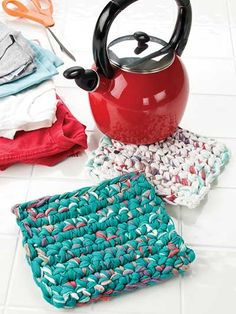 a red tea kettle sitting on top of a kitchen floor next to some crocheted cloths