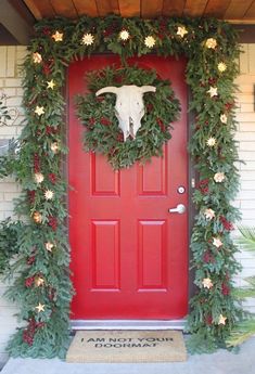 a red door decorated with christmas greenery and a cow's head on it