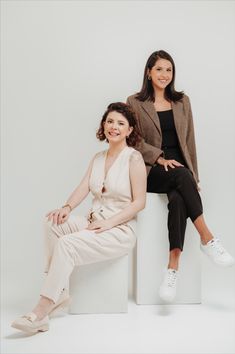 two women sitting next to each other on top of a white box with their legs crossed