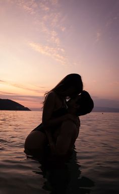 two people are kissing in the water at sunset or dawn, with an island in the background