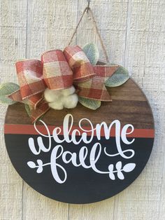 a welcome fall sign hanging on the side of a wooden wall with a bow and plaid ribbon