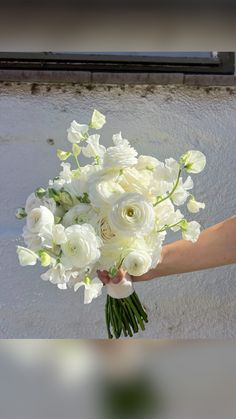 a bouquet of white flowers being held by someone's hand in front of a building