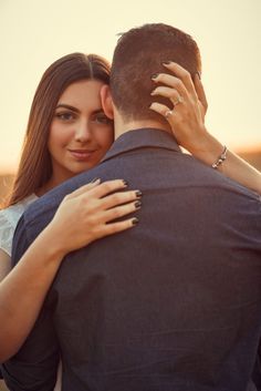 a man and woman embracing each other while the sun is setting