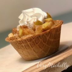 a dessert with whipped cream and fruit in a bowl on a wooden table next to a white wall