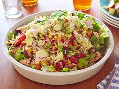 a salad in a white bowl on top of a wooden table next to plates and utensils