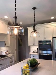 two lights hanging over a kitchen island with fruit on the counter and an oven in the background