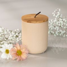 a white vase with a wooden lid next to flowers