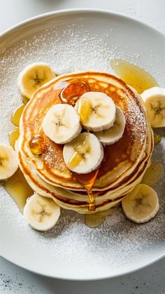 pancakes topped with bananas and syrup on a white plate