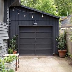 a black garage with lights hanging from the roof and potted plants in front of it