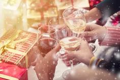 several people holding wine glasses in front of a christmas tree with presents on the table