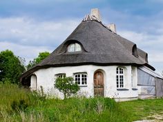 an old thatched roof house with two windows and a door in the grass near some trees