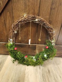 a wreath made out of twigs and moss with lights hanging from the top, sitting on a wooden floor