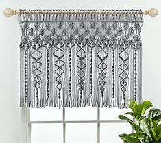 a window curtain with fringes hanging from it's side, next to a potted plant