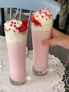 two desserts with strawberries and whipped cream are on a white doily next to a blue chair