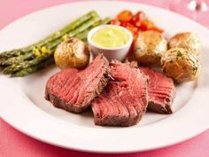 a white plate topped with meat and veggies on top of a pink table cloth