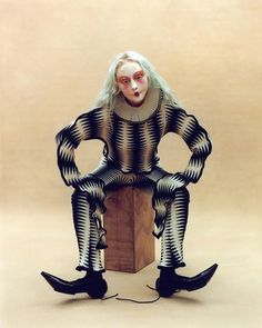 a woman sitting on top of a wooden block wearing black and white striped clothes with her hands in her pockets