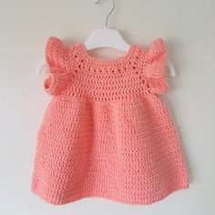 a pink crocheted dress hanging on a white wall next to a hanger