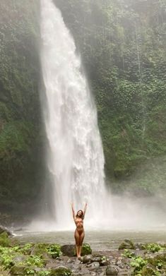 a woman standing in front of a waterfall with her arms up and hands raised above her head