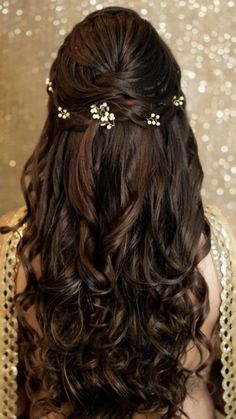 the back of a woman's head with long curly hair and gold accessories on it