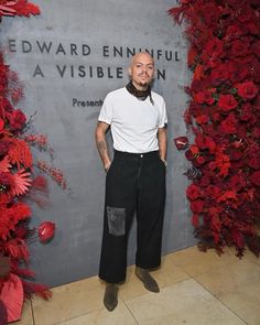 a man standing in front of a wall with red flowers and greenery on it