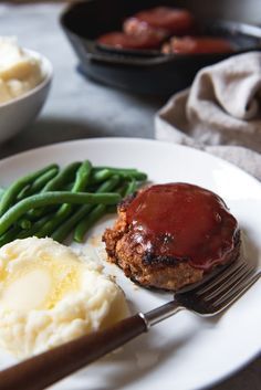 a plate with meatloaf, mashed potatoes and green beans on it next to a fork