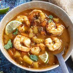 a bowl of soup with shrimp and limes on the side next to a spoon