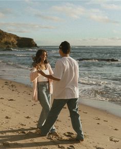 a man and woman are walking on the beach holding hands while looking at the ocean