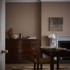 a room with a table, chair and lamp in it next to a door that has a painting on the wall