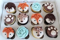 cupcakes decorated with frosting and animal faces are displayed in a white box